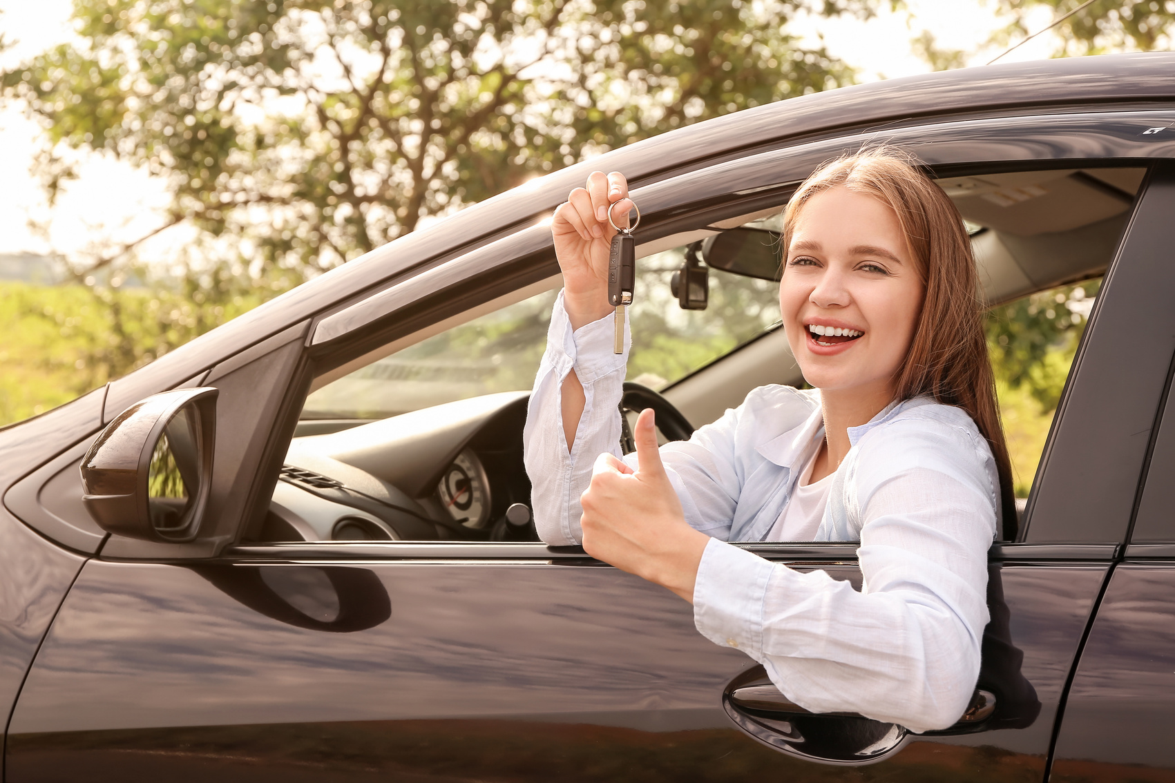 Happy Young Woman with Key Sitting in New Car